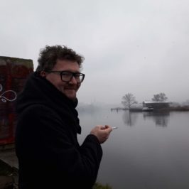 Stanisław Ruksza trzymający tlącego się papierosa na tle zamglonej rzeki