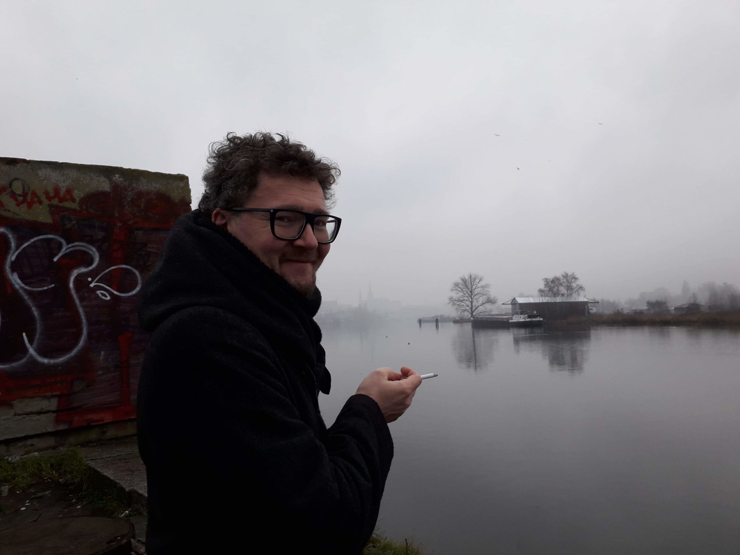 Stanisław Ruksza trzymający tlącego się papierosa na tle zamglonej rzeki